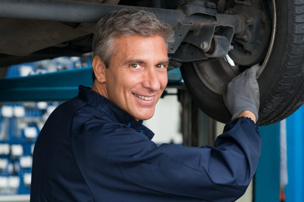 Portrait Of Happy Mature Mechanic At Repair Service Station Changing Tire